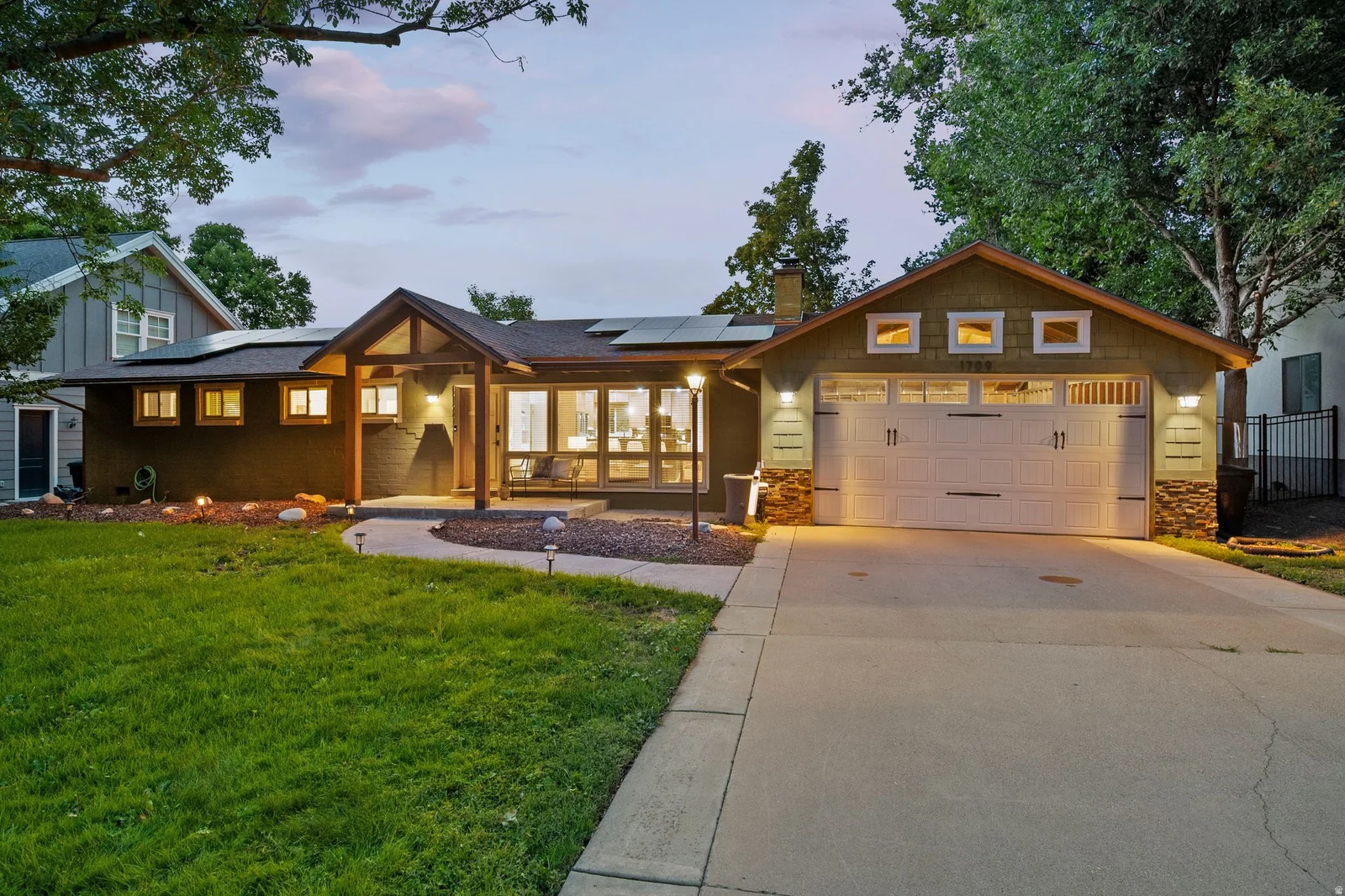 Exterior features a covered entry, multiple window styles, an attached garage with carriage-style doors, and solar panels